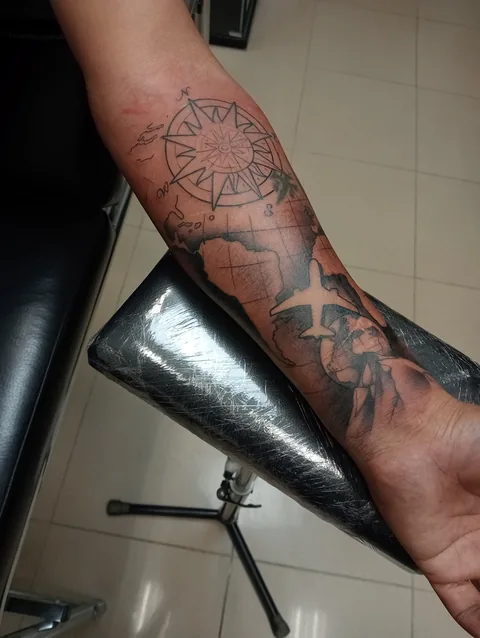 Tatuaje blackwork de una brújula con motivos marinos en el antebrazo.