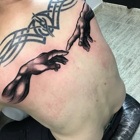 Tatuaje black and grey de las manos de La creación de Adán en el costado.