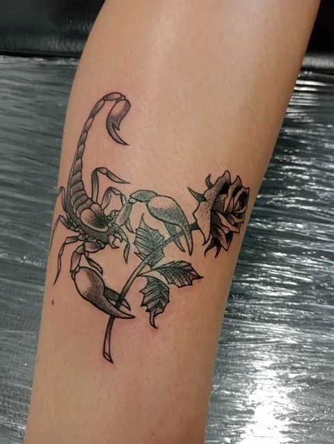 Tatuaje neotradicional de un escorpión entre flores en el antebrazo.
