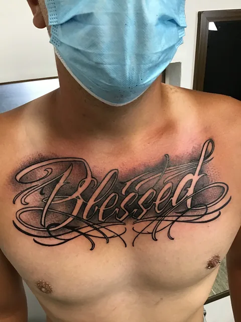 Tatuaje lettering de la palabra Blessed en el pecho.