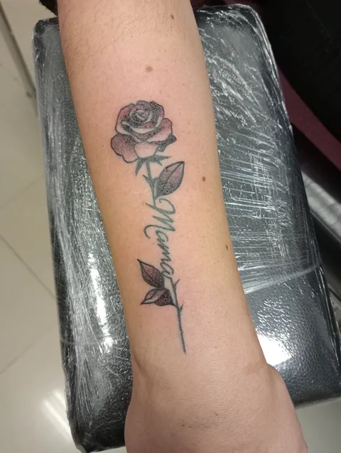 Tatuaje lettering con una rosa de trazo fino en el brazo.