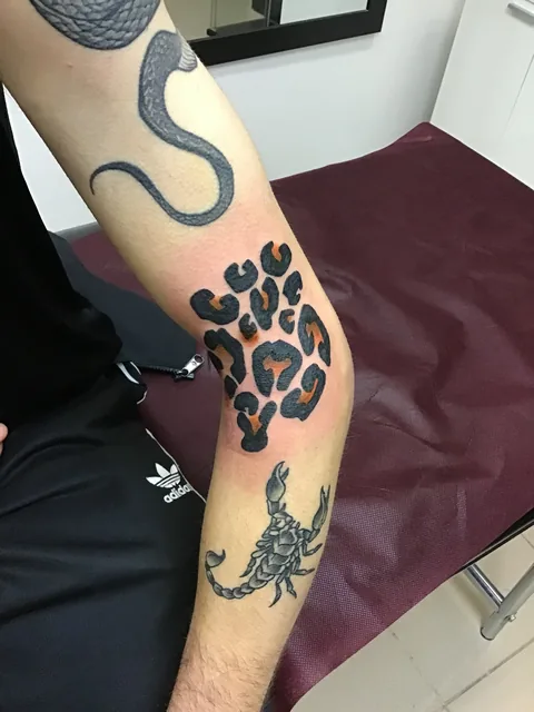 Tatuaje blackwork con manchas de leopardo y un escorpión en el brazo.