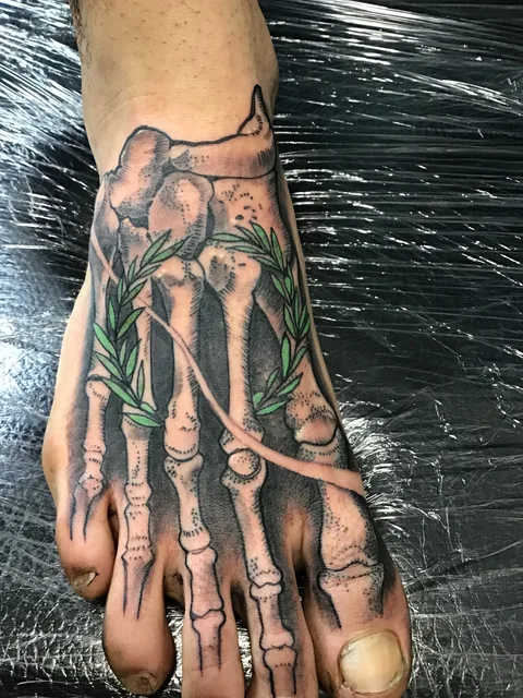 Tatuaje black and grey de una mano esquelética sobre el pie.