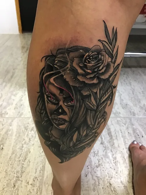 Tatuaje black and grey de una mujer con una rosa en la pierna.