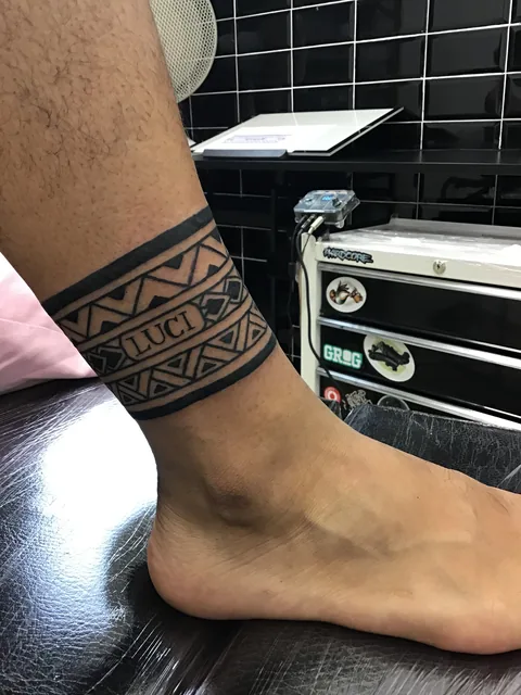 Tatuaje ornamental blackwork con un nombre alrededor del tobillo.