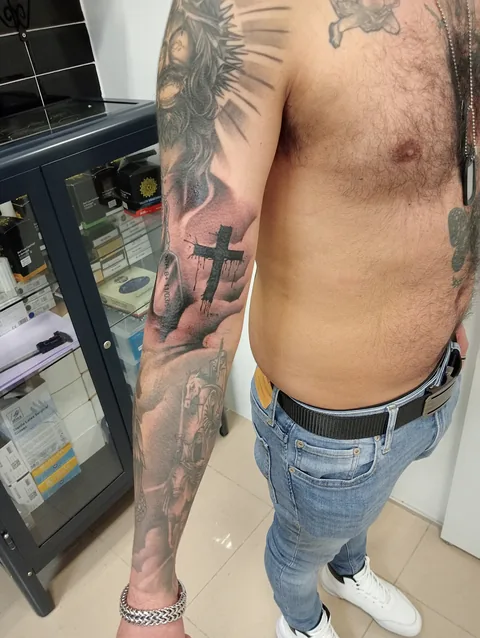 Tatuaje black and grey de temática religiosa con cruces en el brazo.