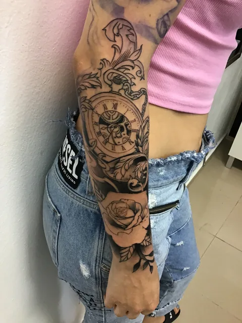 Tatuaje black and grey con reloj y brújula en el brazo.
