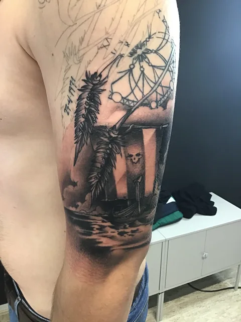 Tatuaje black and grey con reloj y paisaje en el brazo.
