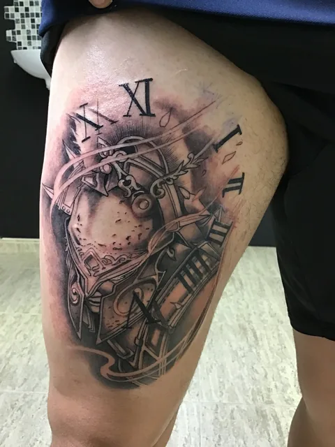 Tatuaje black and grey de un reloj con números romanos y engranajes en el muslo.