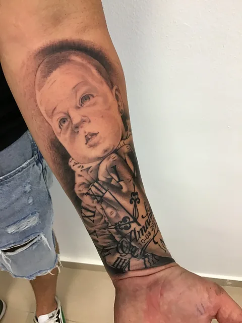 Tatuaje black and grey de un retrato de bebé con una rosa en el antebrazo.