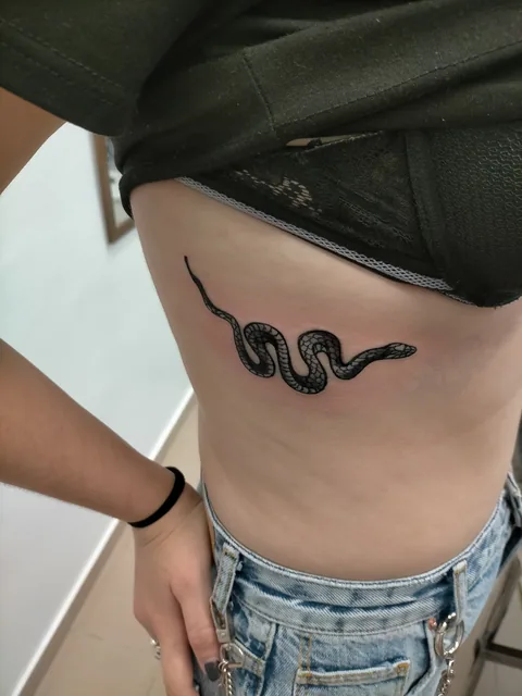 Tatuaje minimalista blackwork de una serpiente en el costado.